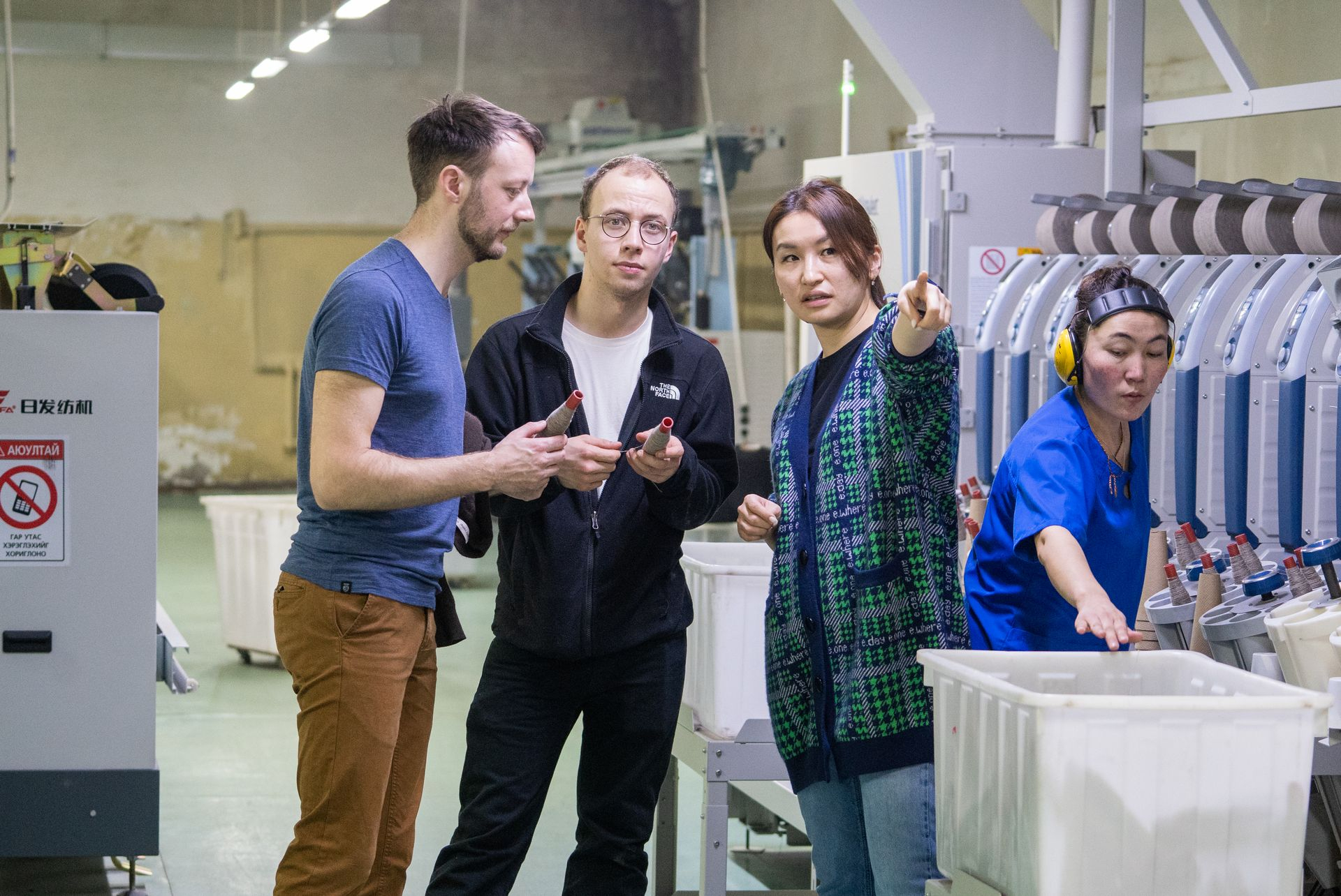 Mehrere Personen stehen in einer Produktionshalle. Eine Frau erklärt den anderen wie die Produktion funktioniert.