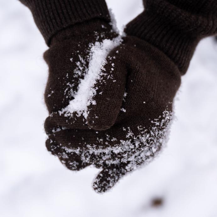 Hände in dunkelbraune Handschuhen aus Yakwolle formen Schneeball