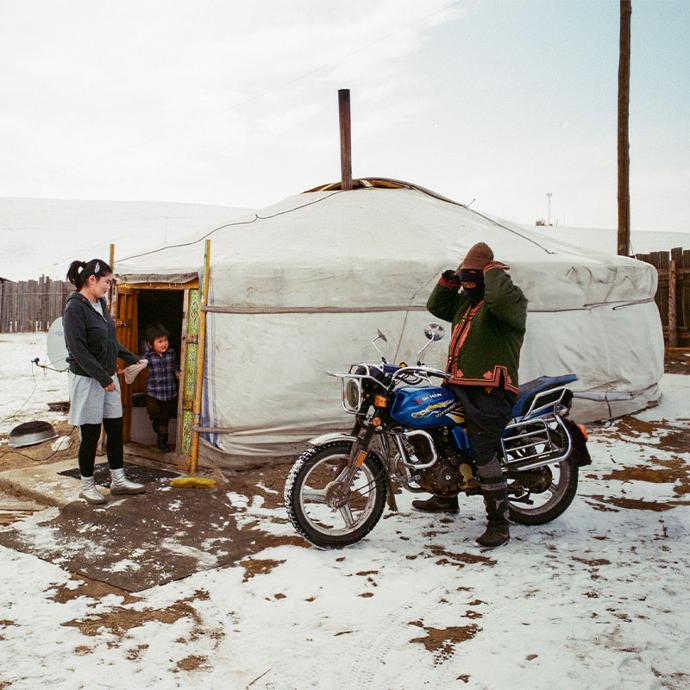 A woman and her son look out of a yurt at a man on a motorcycle