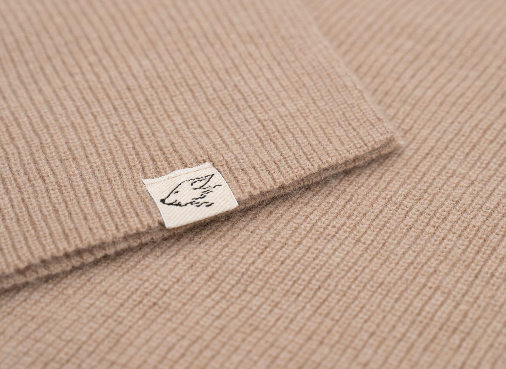 Detail des Saums eines beigen Loose-Fit Pullovers aus Kamelwolle