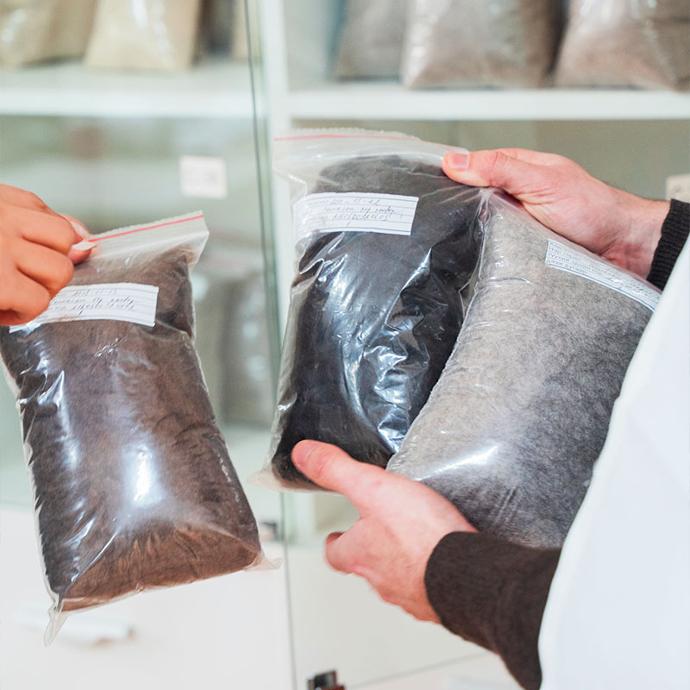 Three plastic bags of raw wool are held up in a laboratory