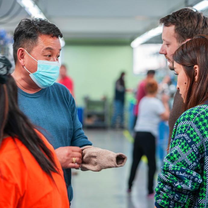 Three people stand in a production hall while one holds a sock.