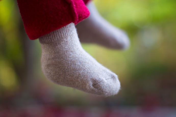 Kinderfüße mit beigen babysocken aus Kamelwolle in herbstlichen Hintergrund.