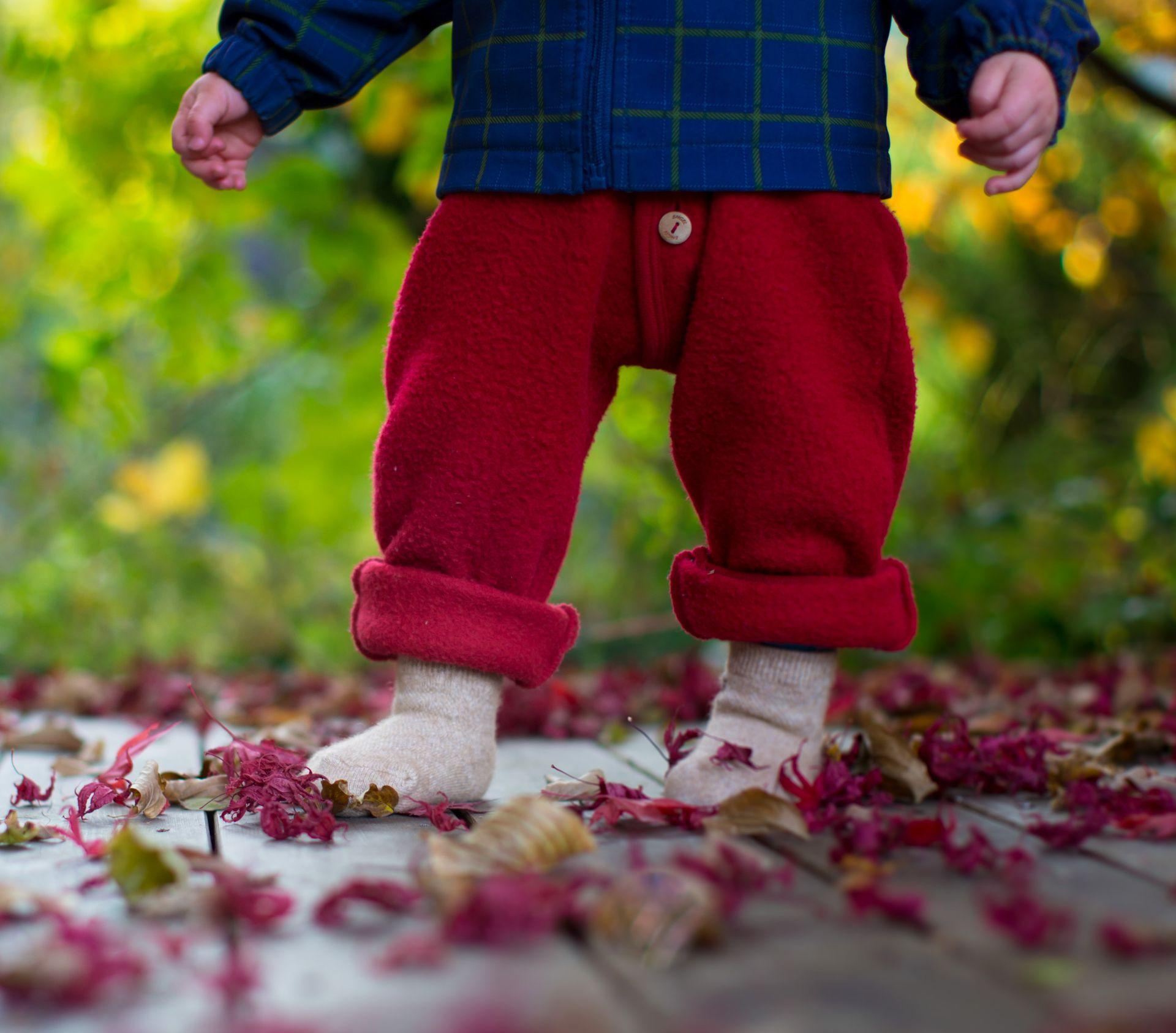 Kind trät beige Kindersocken aus Kamelwolle und steht in herbstlicher Umgebung.