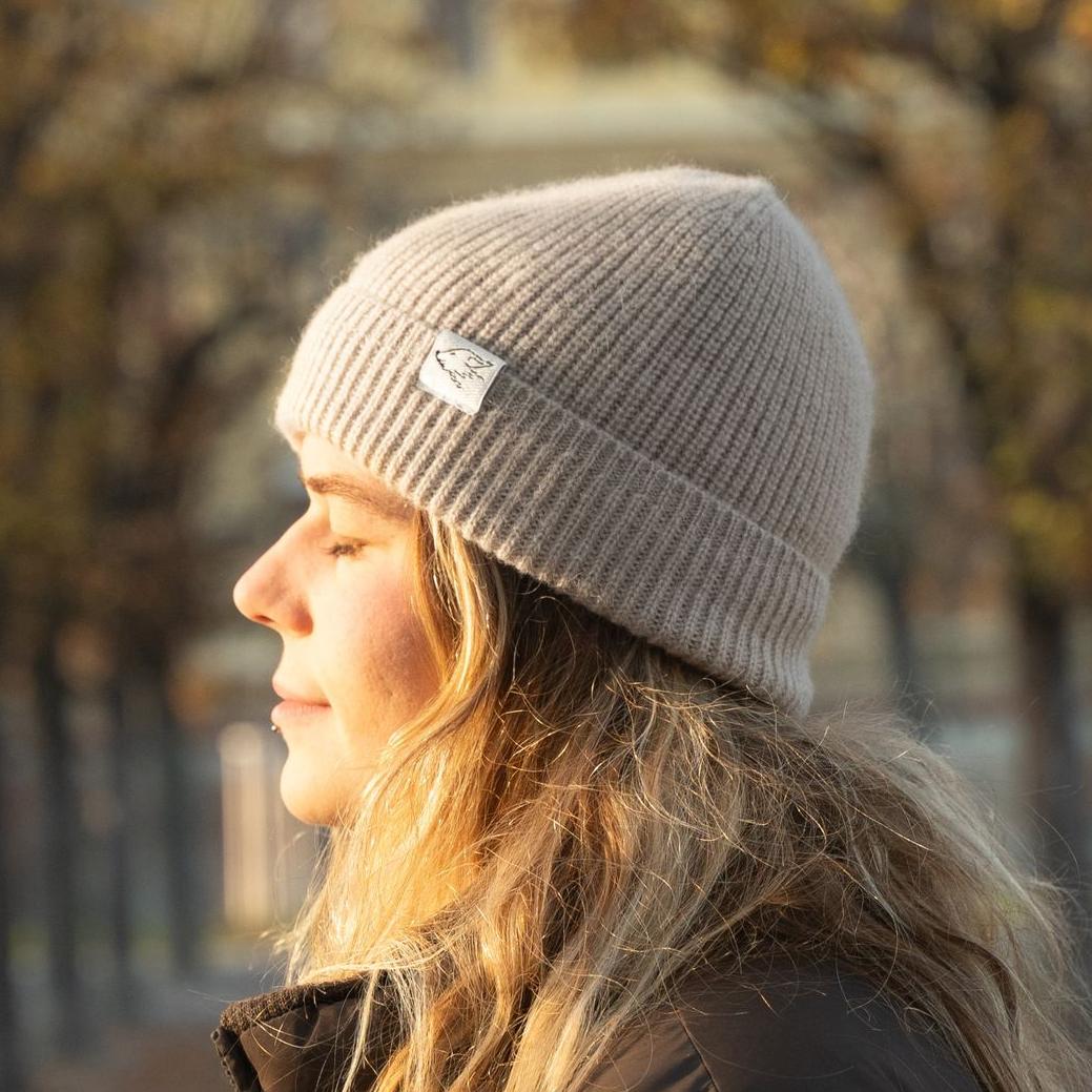 Eine Person mit einem grau gestrickten Beanie, die nach rechts schaut, mit einem verschwommenen Hintergrund im Freien.