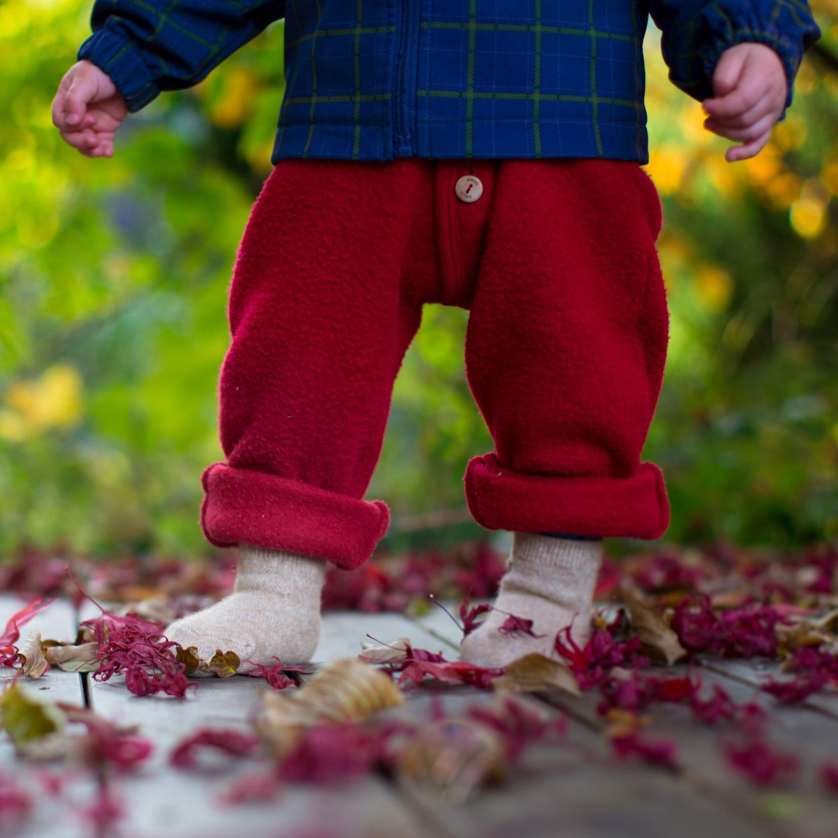 Kinderbeine in roten Hosen und beigen Socken, die auf einem Bett aus Blättern stehen.