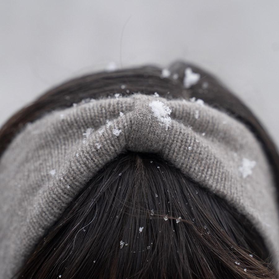 Nahaufnahme des Kopfes einer Person, die ein graues Stirnband trägt, mit Schneeflocken auf dem Haar.