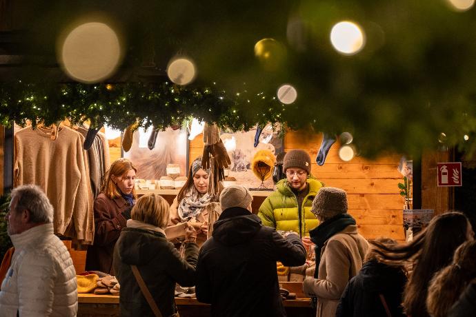 Weihnachtsmarktstand mit Kunden und drei Personen die Wollprodukte verkaufen