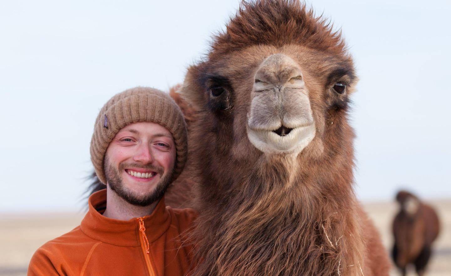 Malte bei seinem Mongoleibesuch 2019 Ein Mann steht lachend neben einem Kamel