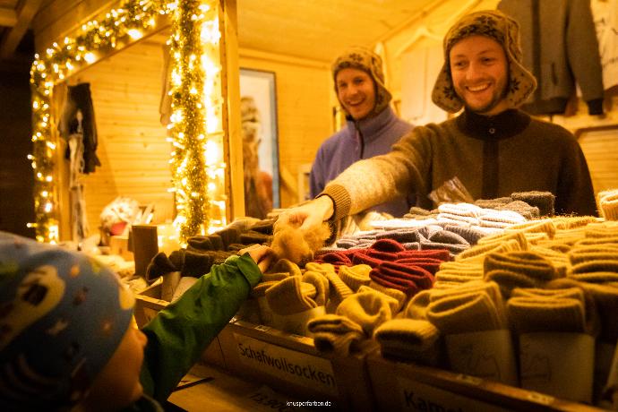 Der erste Weihnachtsmarkt in Düsseldorf Benrath Ein warm beleuchteter Weihnachtsmarktstand mit Wollsocken an dem ein Kind an Wolle fühlt