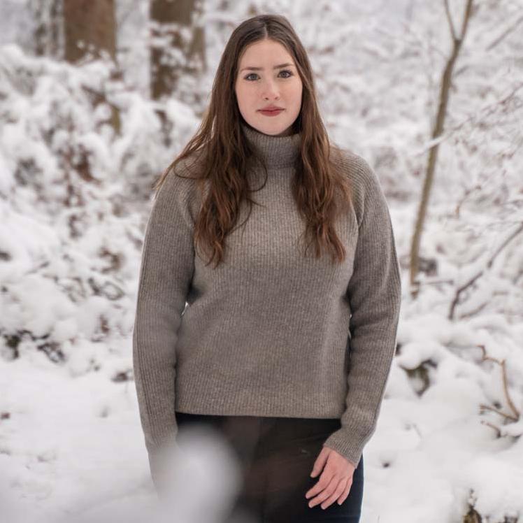 Frau steht in grauem Wollpulli im Schnee