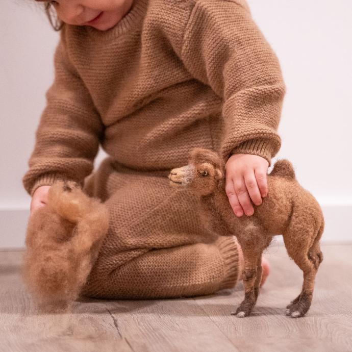 Kleinkind in weichem Pullover aus Kamelwolle spielt mit einem Stofftier.