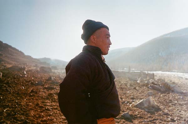 Ein Mann steht im Gegenlicht vor Bergen und Schnee auf Gras