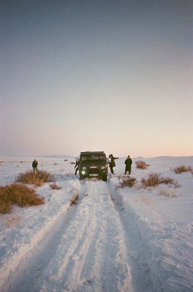 People next to a minibus in a snowy landscape at sunset