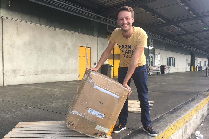 Ein junger Mann kippt ein großes Paket auf der Ladefläche einer Abholstation.