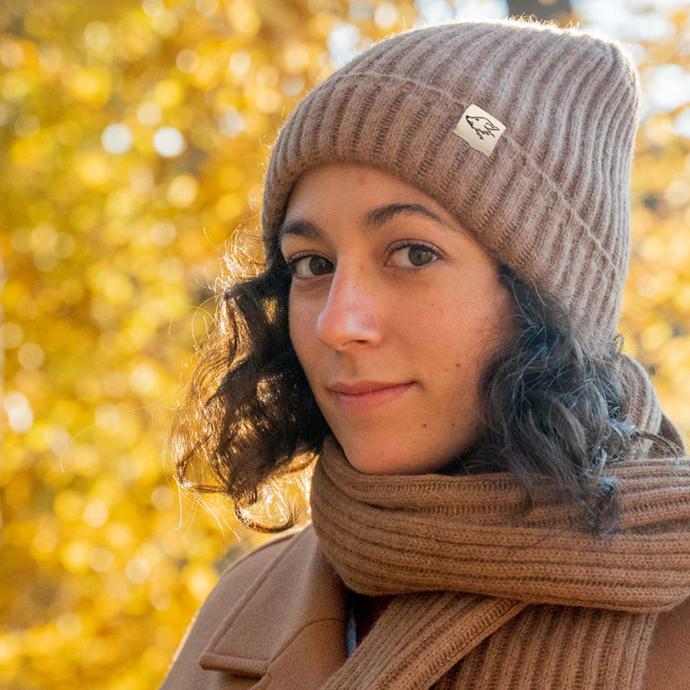 Woman with dark curls wears a brown woollen hat