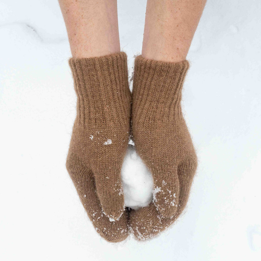 Braune Handschuhe aus Wolle halten einen Schneeball