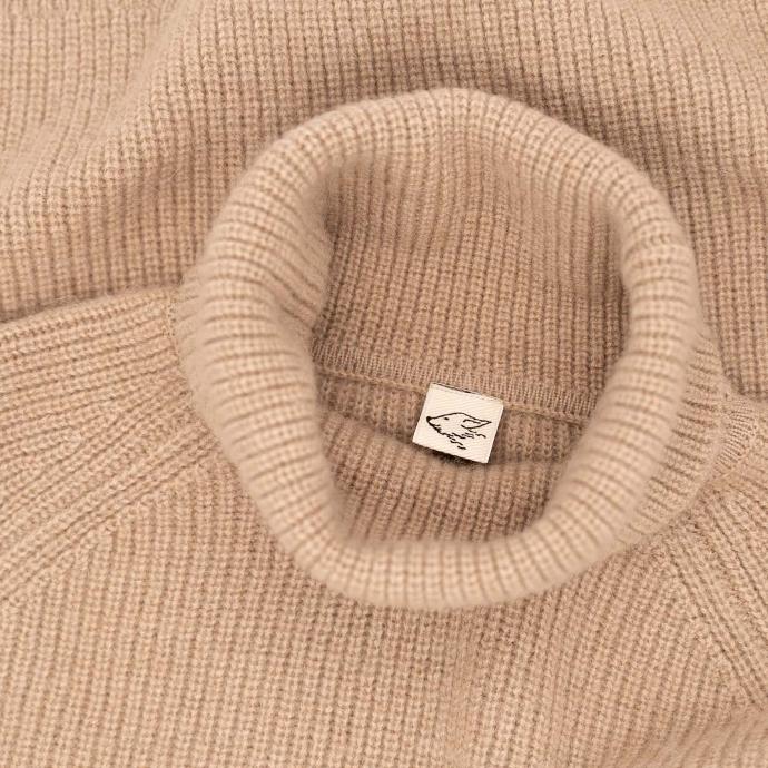 Kragen eines beigen Rollkragenpullover mit steppenstrolch Logo im Nacken